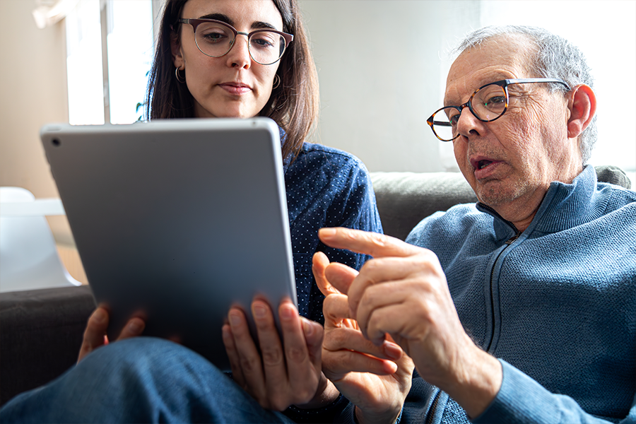 A young woman and older man are in discussion and are both looking at a tablet screen.