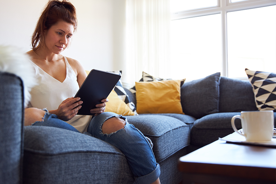 Young woman on a blue sofa looking at a tablet screen.