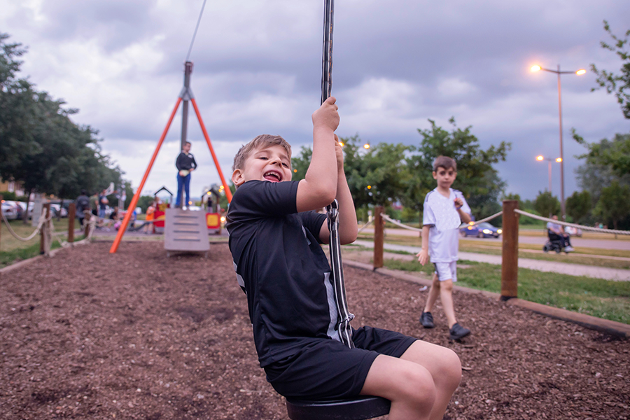 Three small boys in a park. One is on a zipwire and smiling broadly.